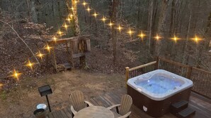 Terraza exterior con jacuzzi, sillas de madera, una mesa y guirnaldas de luces.