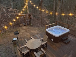 Terraza exterior con jacuzzi, sillas de madera, una mesa y guirnaldas de luces.