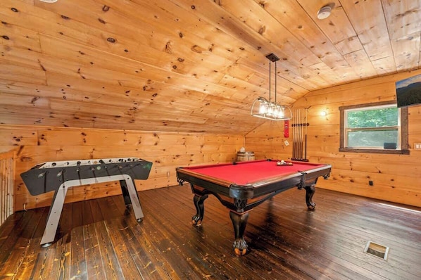 Una sala con paneles de madera, mesa de billar y mesa de futbolín.