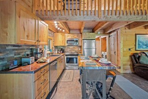 Una cocina moderna con armarios de madera, una isla central, electrodomésticos de acero inoxidable y una zona de estar con sofá y mesa.