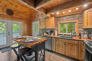 A wooden cabin interior with a kitchen area featuring a dining table, bar stools, and a stone backsplash.