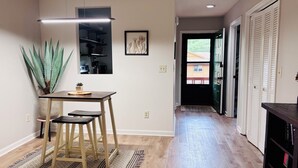 Une cuisine moderne avec un plancher en bois, une table à manger avec des tabourets, un luminaire suspendu et une plante en pot.