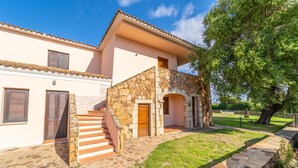 A two-story stone house with a stone staircase leading to the upper floor, a stone entrance, and a well-maintained lawn. - Appartamenti Le Carrube vicini al mare (San Teodoro)