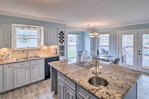 A modern kitchen with granite countertops, white cabinetry, and a large island with a sink. - Waterfront San Jacinto River Home w/ Boat Slip! (Houston)