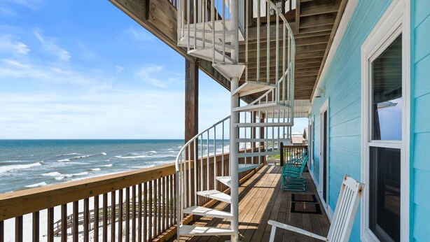 A wooden deck with a spiral staircase, a view of the ocean, and a building with a blue exterior. - Big Blue Heaven: Gorgeous Gulf Views, Swim Spa, 7 Bedrooms! (Cape San Blas)
