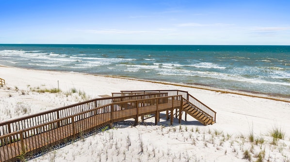 Une promenade en bois qui mène à la plage, avec du sable et une végétation clairsemée.