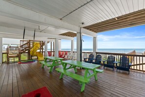 A covered deck with picnic tables and chairs, a slide, and a view of the ocean.