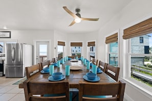 Un espace repas avec une longue table dressée pour accueillir plusieurs personnes, un ventilateur de plafond et une vue sur l’extérieur.