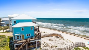 A two-story beach house with a wooden deck, a staircase leading to the upper floor, and a view of the ocean.