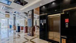 A modern lobby with a marble floor, a reception desk, a black wall with a decorative panel, and an elevator. - Luma Serviced Apartments (Madinah)