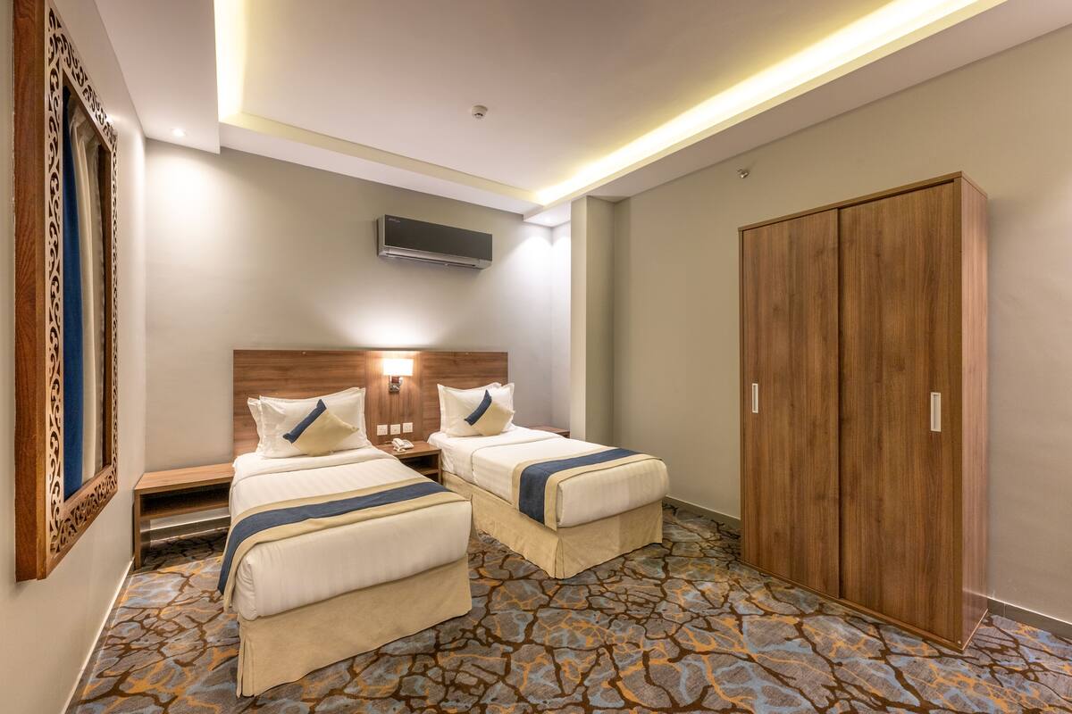 A hotel room with two beds, a wardrobe, a flat-screen TV, and a patterned carpet.