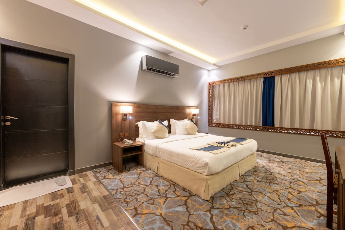 A hotel room with a bed, bedside table, lamp, air conditioning unit, and a large mirror.