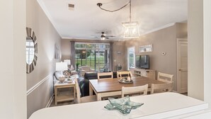 A dining area with a wooden table, chairs, a ceiling fan, and a television.