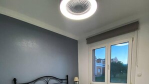 A bedroom with a bed, a nightstand, a lamp, a window, and a ceiling light.
