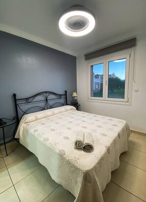 A bedroom with a bed, a nightstand, a lamp, a window, and a ceiling light. - Solea Mare by Midelisa (oliva nova golf)