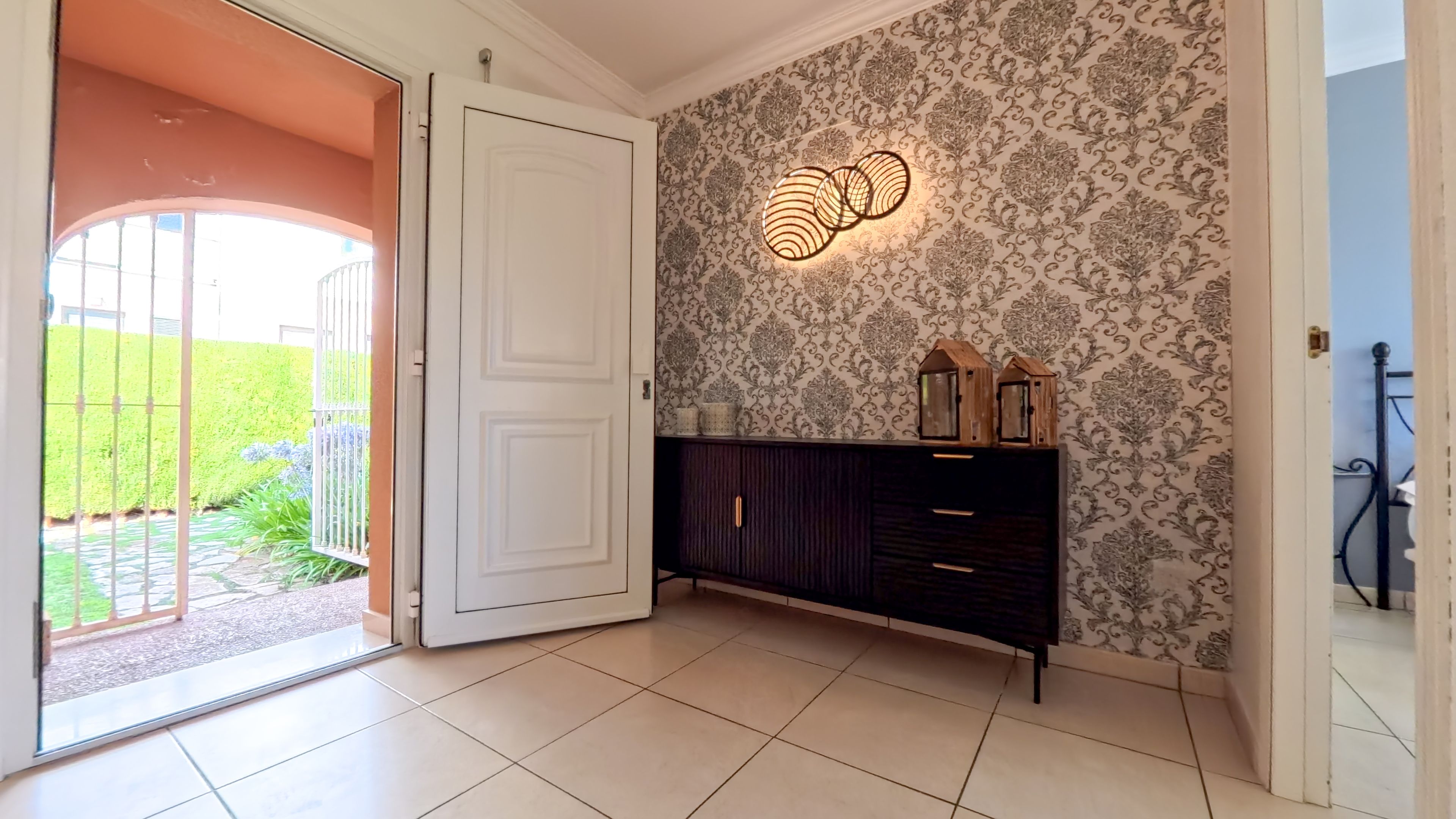 Ein Zimmer mit gemustertem Wandpapier, einer dunklen Holzkabine mit Schubladen und einer Tür zu einem Außenbereich.