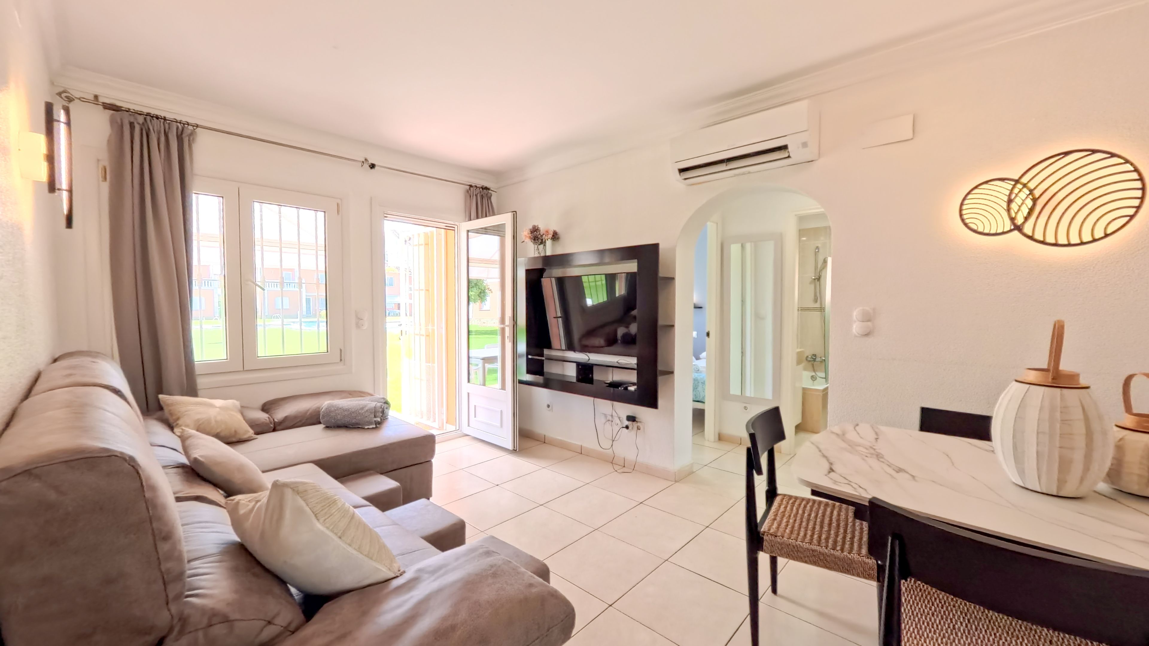A modern living room with a sofa, TV, and a dining area with a table and chairs.