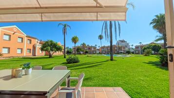 Un patio con mesa y sillas, una piscina y vistas a una zona residencial con casas y palmeras.