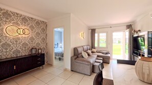 A modern living room with a sofa, a TV, and a decorative wall. - Solea Mare by Midelisa (oliva nova golf)