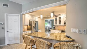 A kitchen with a large island, bar stools, white cabinets, stainless steel appliances, and pendant lighting. - Screened-In Private Pool: Waterfront Home (Cape Coral)