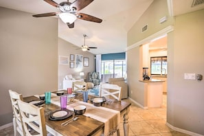 A dining area with a wooden table set for four, a ceiling fan, and a view into the kitchen.
