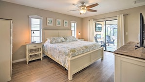 A bedroom with a bed, a nightstand, a ceiling fan, and a view of the outdoors. - Screened-In Private Pool: Waterfront Home (Cape Coral)