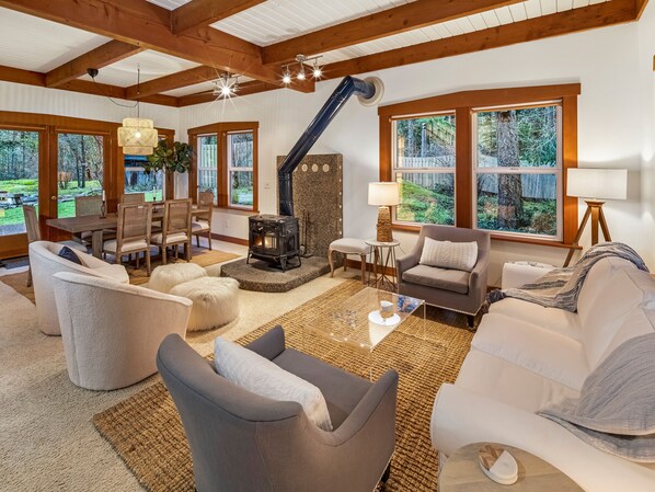 A cozy living room with a fireplace, comfortable seating, and large windows offering a view of the outdoors.
