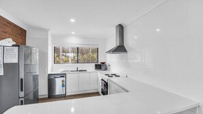 Une cuisine moderne avec des meubles blancs, un réfrigérateur en acier inoxydable, un four à micro-ondes, une cuisinière et une grande fenêtre.