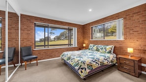 A bedroom with a large bed, two windows, a chair, and a nightstand. - Cuttagee Beach Cottage 6 - Tathra Bermagui Rd 3521 (Barragga Bay)