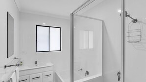 Un bany modern amb un tramant de dutxa de vidre, un lavabo amb mirall i una finestra.