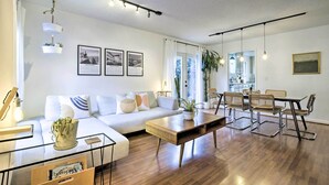 Ein modernes Wohnzimmer mit einer Couch, einem Esstisch und Stühlen. An der Wand hängen gerahmte Bilder und auf dem Tisch steht eine Pflanze.