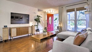 Ein Wohnzimmer mit Holzboden, einer Couch, einem an der Wand montierten Fernseher und einer Treppe, die in einen anderen Raum führt.