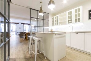 Una cocina moderna con armarios blancos, una isla central con taburetes, iluminación colgante y vista al área de comedor.