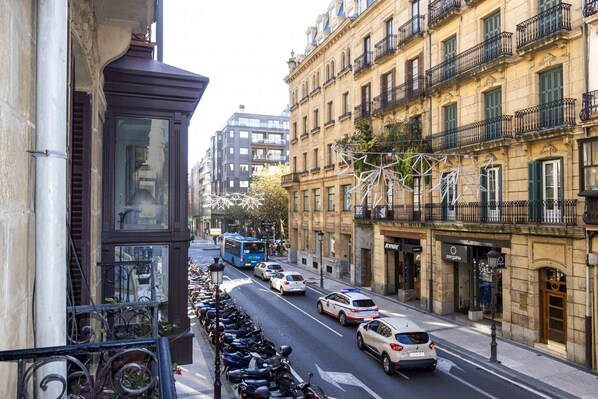 Vista de la calle con coches estacionados, un autobús y edificios con balcones.