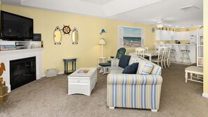 A living room with a fireplace, a television, a striped sofa, and a dining area with white cabinets. - 3 Br with pool midtown steps to beach, restaurants and amusements (Ocean City)
