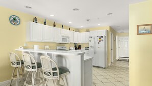 A kitchen with white cabinets, a central island with bar stools, a microwave, and a refrigerator. - 3 Br with pool midtown steps to beach, restaurants and amusements (Ocean City)