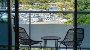 A balcony with two chairs and a small table, overlooking a marina with boats and a coastal landscape. - The Watermark (WM1102) Luxury 11th-floor 2 BDR, balcony, AC, remote work (Honolulu)