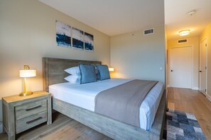 A bedroom with a wooden bed, two bedside tables, a nightstand, and a wall-mounted lamp.