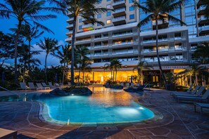 A hotel with a swimming pool surrounded by lounge chairs and palm trees.