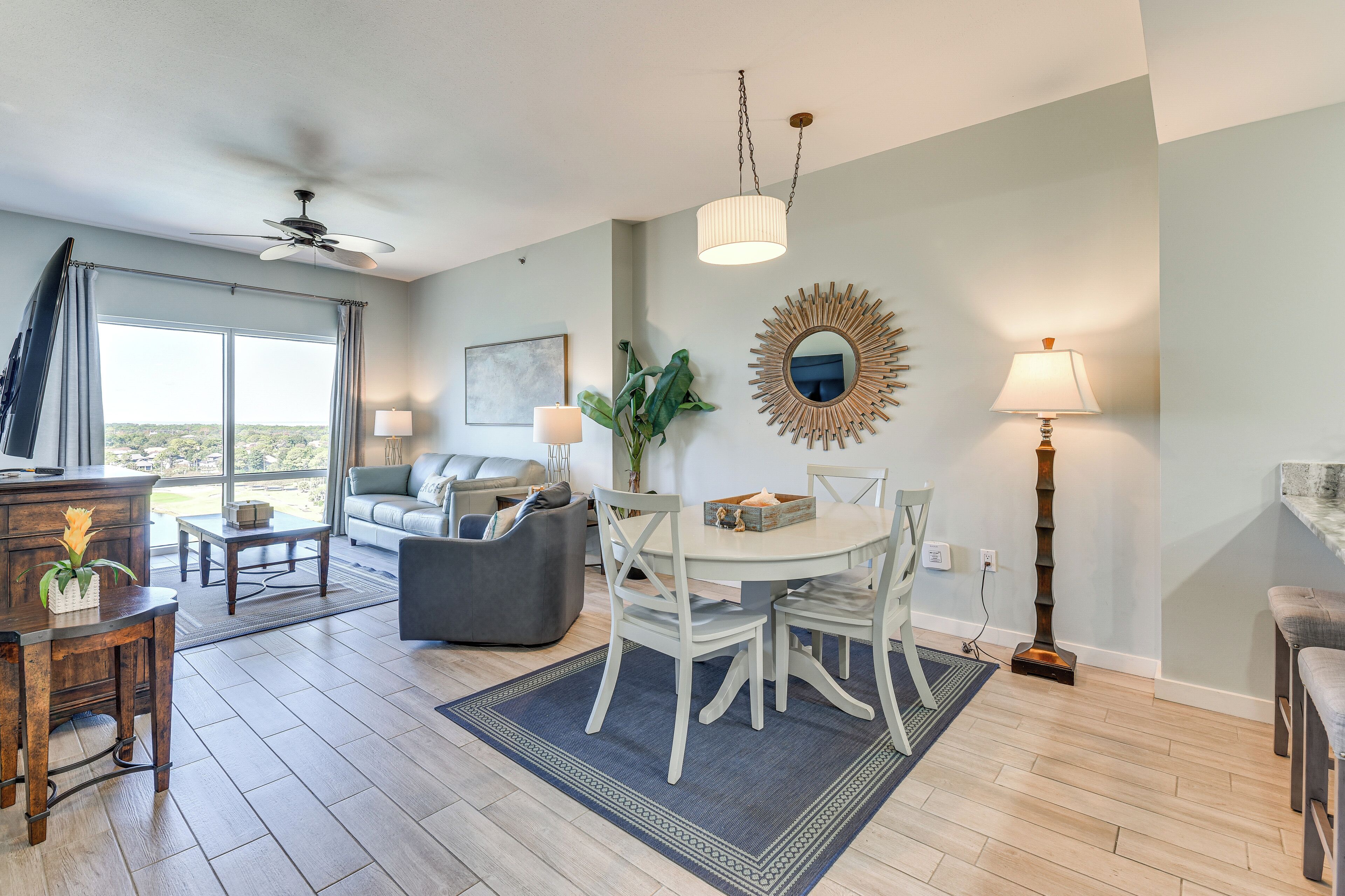 A modern living room with a dining area, a ceiling fan, a large window, and a decorative mirror.