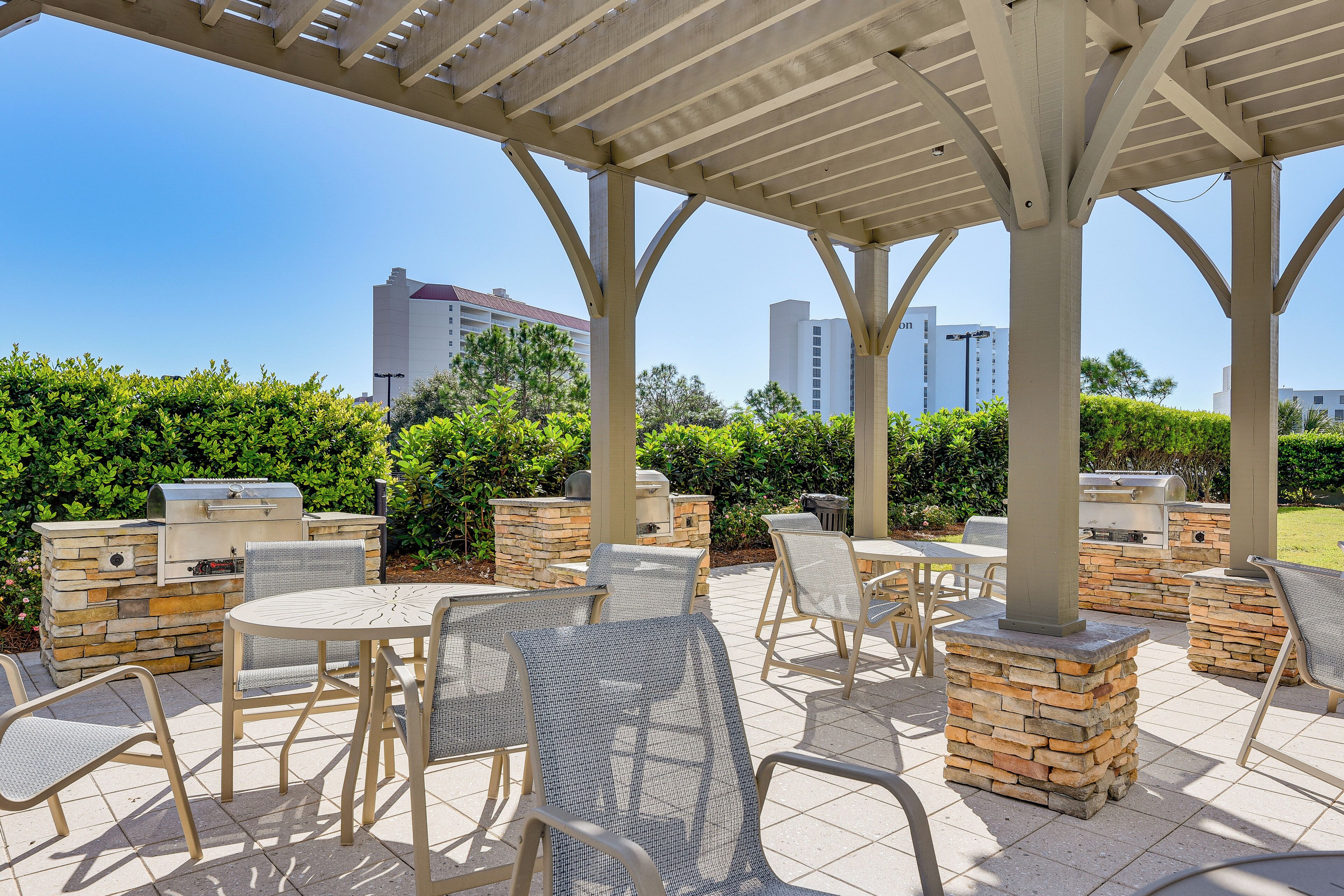 An outdoor patio area with stone pillars, metal chairs, and a grill.