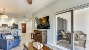 A spacious living room with a sofa, coffee table, and a television. There is a sliding glass door leading to a balcony with wicker furniture. - Balcony & Views! 'Beach Bliss' in Sandestin Resort (Destin)