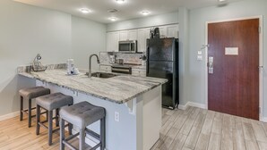 A modern kitchen with a central island, bar stools, stainless steel appliances, and a wooden door. - Balcony & Views! 'Beach Bliss' in Sandestin Resort (Destin)