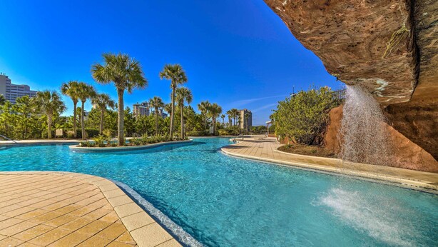 A swimming pool with clear blue water, surrounded by palm trees and a rocky cliff. - Balcony & Views! 'Beach Bliss' in Sandestin Resort (Destin)