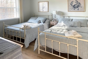 A bedroom with two single beds, a bedside table with a lamp, and a framed seahorse artwork on the wall.