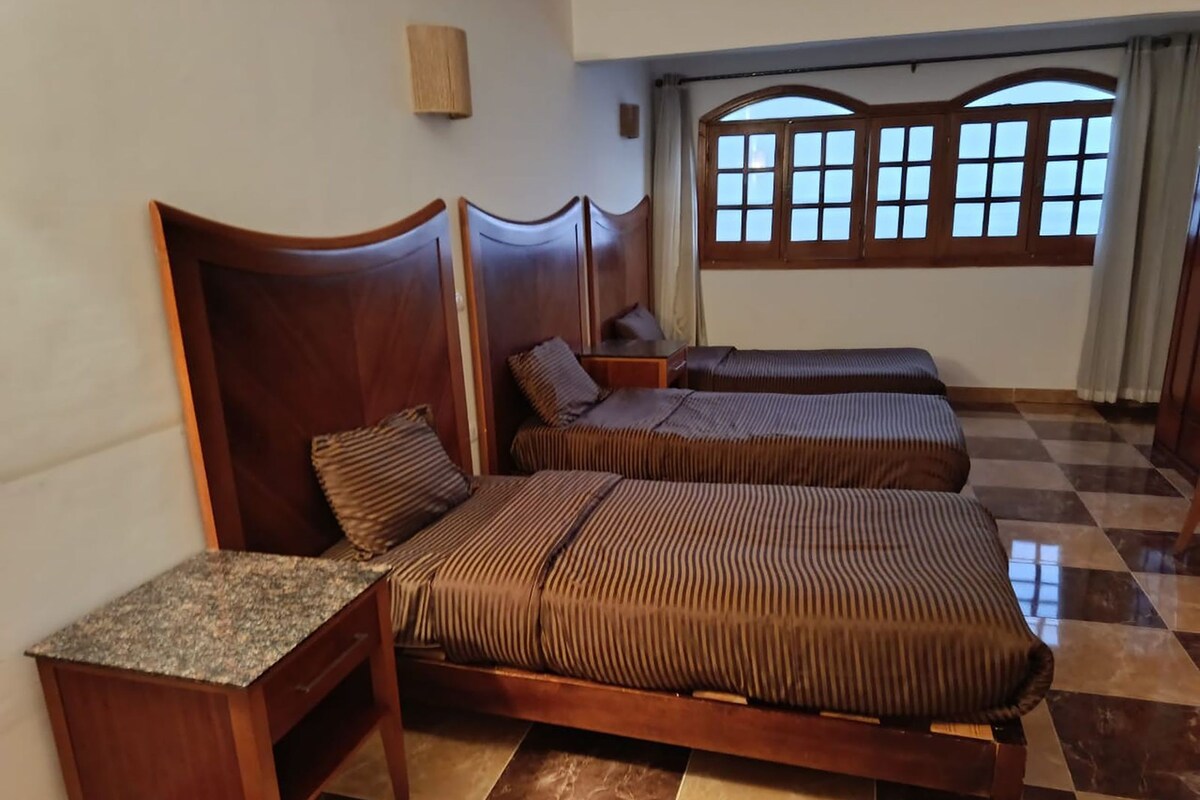 A room with two beds, a nightstand, and a window with curtains.