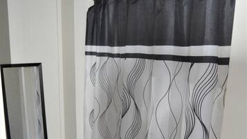 Une salle de bain avec un rideau de douche orné d’un motif ondulé, un tapis noir et un miroir au mur.