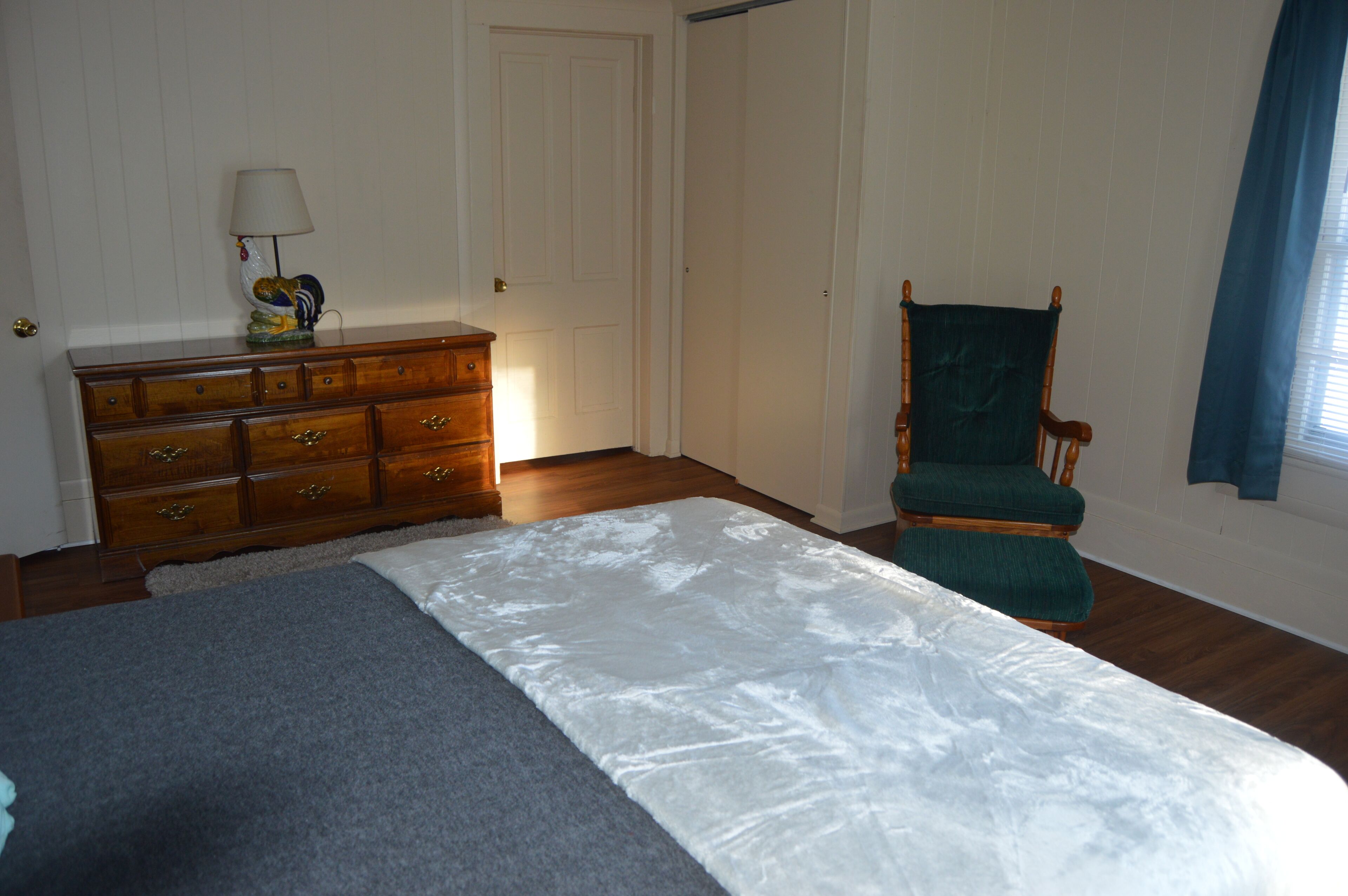 Un dormitorio con cama, cómoda, silla y puerta.