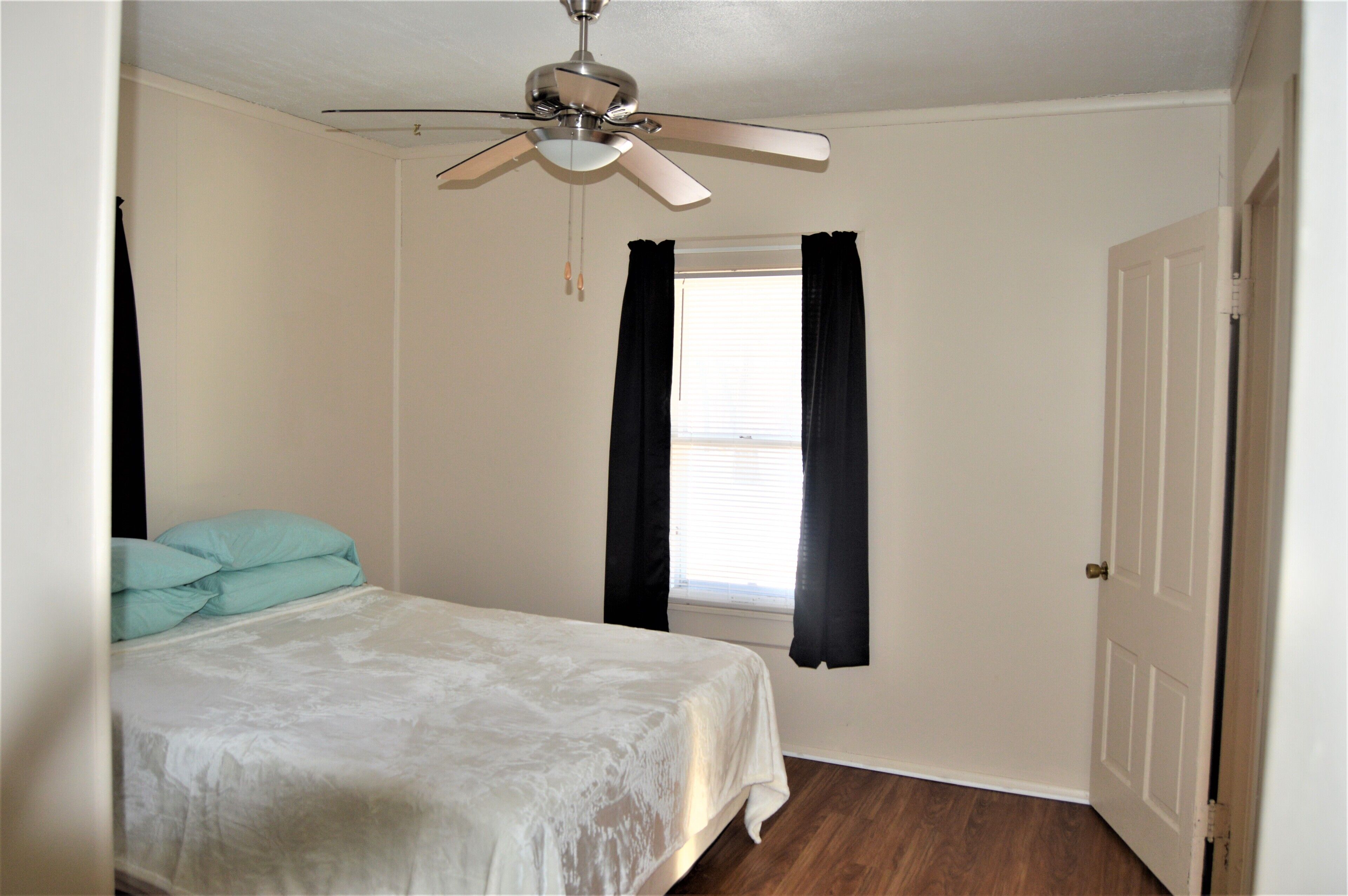 A bedroom with a bed, a ceiling fan, a window with curtains, and a door.