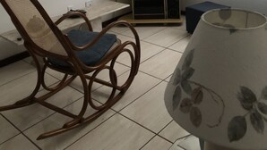 A room with a television on a stand, a rocking chair, a lamp, and a mirror on the wall. - Near Praia do Forte - second block (Cabo Frio)